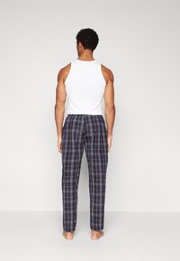 Pijamale pentru bărbați, cu un top alb fără mâneci și pantaloni în carouri de culoare albastru închis, mov și alb. Materialul pare moale, cu un elastic în talie.