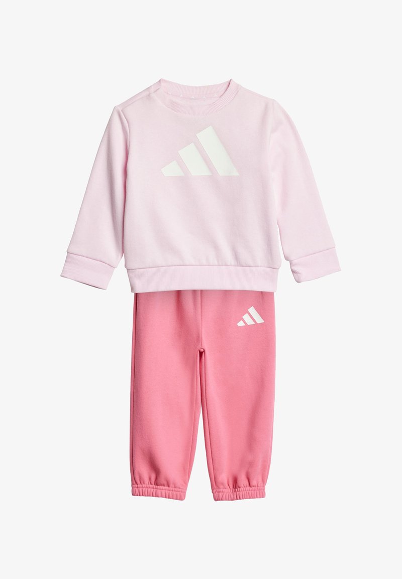 Roze sweatshirt en bijpassende joggers van zacht materiaal. Sweatshirt met wit Adidas-logo; joggers hebben logo op het linkerpijp.