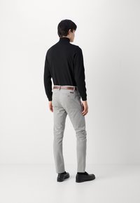 Czarna koszulka polo z długim rękawem, jasnoszare chinosy z brązowym paskiem, czarne buty, model odwrócony plecami na tle białej ściany.
