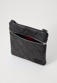 Schwarze, strukturierte Leder Tasche mit einem gesteppten Design. Verfügt über einen silbernen Reißverschluss und ein rotes Innenetikett mit dem Markennamen.