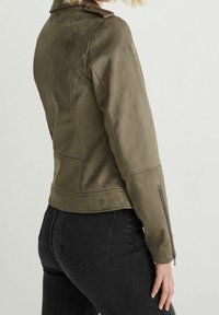 Veste en simili cuir vert olive avec une coupe légèrement cintrée, dotée de manches à zip et de détails en panneau. Texture mate avec une finition douce.