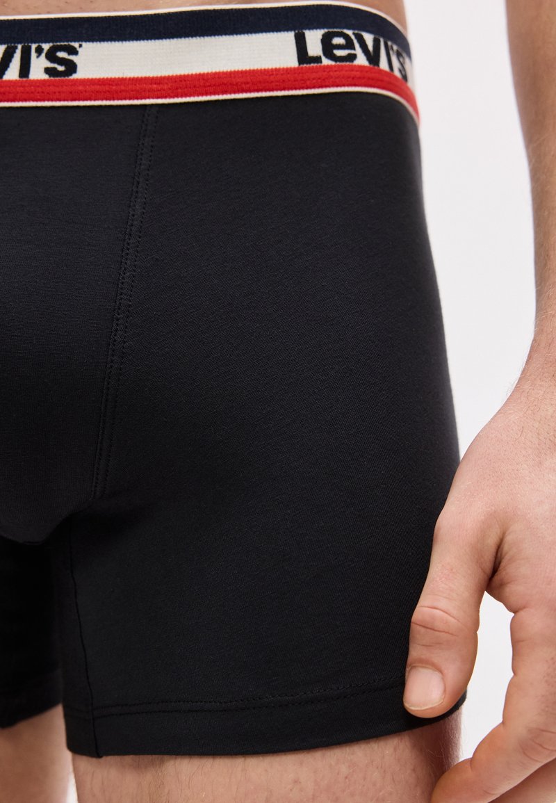 Close-up of black Levi's boxer briefs on a person, featuring a branded waistband with red and white stripes and a visible hand at the side.