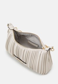 Sac à main plissé beige avec quincaillerie dorée, fermeture éclair et doublure intérieure lisse, présentant une étiquette à l'intérieur et une forme arrondie.