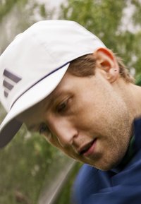 Casquette blanche avec des accents marins, arborant un logo sur le devant. Le tissu semble lisse et léger, idéal pour les activités en extérieur.