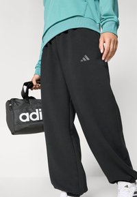 Svart joggebukse med avslappet passform, med en subtil Adidas-logo. Kombinert med en turkise sweatshirt og en svart treningsbag med hvit merkevare.