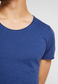 Blå kortärmad T-shirt med rund hals, tillverkad av ett slätt, strukturerat tyg. Färgen är enfärgad, utan synliga mönster eller detaljer.