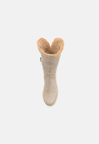 Bota de ante beige con un forro de pelo sintético suave y crema asomando por la parte superior, y una cremallera lateral para facilitar el uso. Punta redondeada y suela de goma.