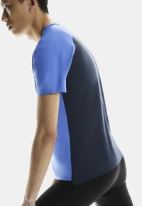 Koszulka sportowa z krótkim rękawem, z niebieskim przodem i ciemnoniebieskim tyłem. Wykonana z teksturowanej tkaniny odprowadzającej wilgoć, z luźnym krojem.