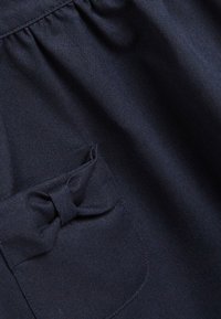 Marinbl�ått tyg med en strukturerad yta, med en rynkad midja och en ficka som är prydd med en liten båtdetalj.