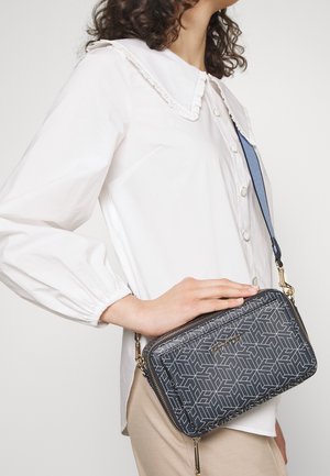 Gray, geometric-patterned crossbody bag with gold hardware and zip closure. Adjustable shoulder strap, features a sleek design and texture.