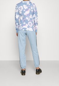 Långärmad blommönstrad topp i blått med vita och lila blommor, tillsammans med ljusblå joggers med svarta sidostråk och elastiska mudd.