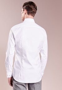 Camisa blanca de manga larga con cuello clásico, corte entallado y puños con botones, confeccionada en tela suave, presentada sobre un fondo neutro.
