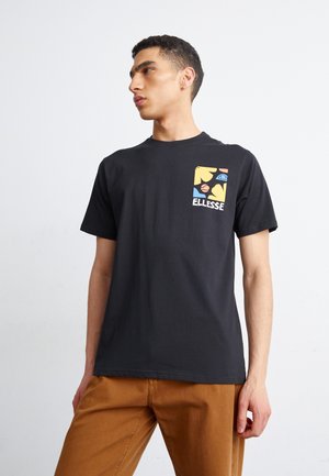 Camiseta de algodón negra con un logo gráfico colorido en el área del pecho izquierdo, combinada con pantalones beige. Mangas cortas y cuello redondo.