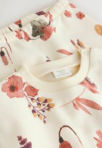 Primer plano de ropa de bebé color crema con patrones florales rosas y naranjas, mostrando cuello acanalado y detalle de botón a presión.