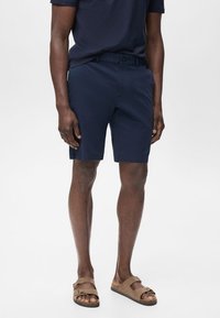 Marina blå bomullsshorts med rak front, sidofickor och knappstängning. Bärs med bruna sandaler och en matchande topp.