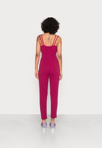 Tuta fucsia con spalline sottili e vita aderente. Presenta una zip nascosta sul retro e una gamba dritta. Accentata con tacchi quadri lavanda.