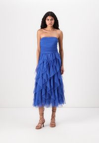 Strapless blue dress features a fitted bodice and a layered tulle skirt with ruffled texture. Paired with strappy tan sandals.