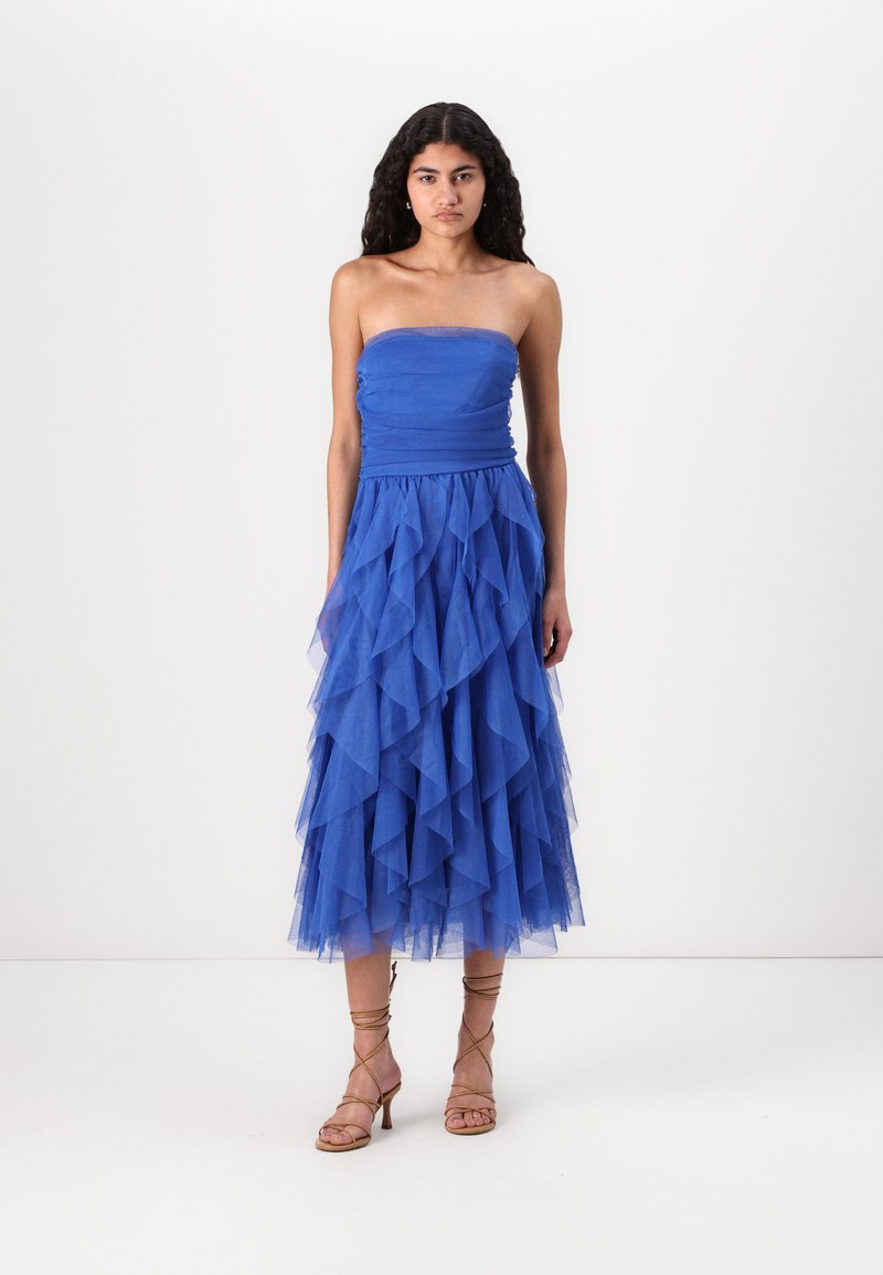 Strapless blå kjole med en tettsittende overdel og en lagdelt tyllskjørt med volangtekstur. Kombinert med sandaler med stropper i tan.