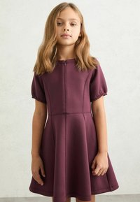 Bourgognefarvet kortærmet kjole i glat stof med tætsiddende bodice og udvidet nederdel med sømdetaljer og lynlåslukning bagpå.