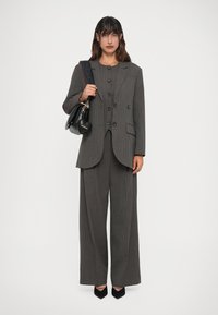 Γκρι κοστούμι ρίγας με διπλό κούμπωμα και παντελόνι με φαρδιά πόδια, συνδυασμένο με μια μικρή μαύρη τσάντα και μαύρες γόβες με μυτερή μύτη.