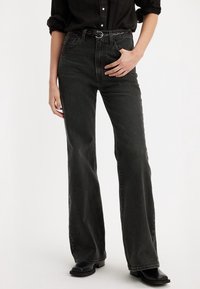 Jean en denim noir taille haute avec des jambes évasées, une ceinture tissée texturée, une finition légèrement décolorée et un design classique à cinq poches.