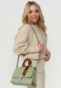 Groene leren handtas met een gestructureerd ontwerp, voorzien van een bruine satijnen linthandgreepaccent, zilveren hardware en een sluiting met flap aan de voorkant.