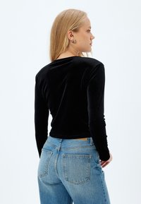 Top a maniche lunghe in velluto nero con scollatura tonda, abbinato a jeans azzurri chiari e sbiaditi. L'outfit presenta un design aderente.