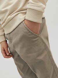 Beige ribbad huppari, jossa on resorit hihansuissa, yhdistettyinä vaaleanharmaisiin housuihin, joissa on sivutasku, sileä pinta ja rento istuvuus.