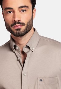 Lichtbeige overhemd met knopen, gemaakt van gladde stof. Het heeft een omgeslagen kraag, subtiele zakdetails en een klein logo op de borst.