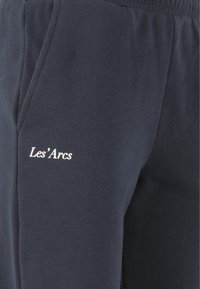 Marinblå sweatsbyxor i bomull med en mjuk textur, med en vit logotyp "Les'Arcs" på vänster sida och sidofickor.