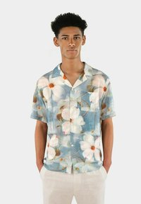 Kortärmad skjorta i lätt material med blommönster som har stora vita blommor på en blå bakgrund, enkel bröstficka, knapplås.