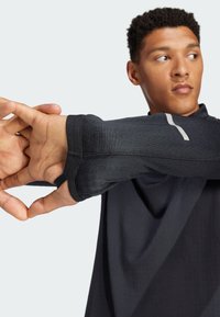 Zwarte sportshirt met lange mouwen en duimgaten, voorzien van een reflecterende grijze accent op de mouw. Gladde textuur en een aansluitend ontwerp.