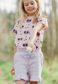 Vaaleanpunainen t-paita, jossa on kissakuviot ja tassunjälkiä; laventelinraidalliset shortsit, joissa on röyhelöitä ja nuppineulan yksityiskohta vyötäröllä.