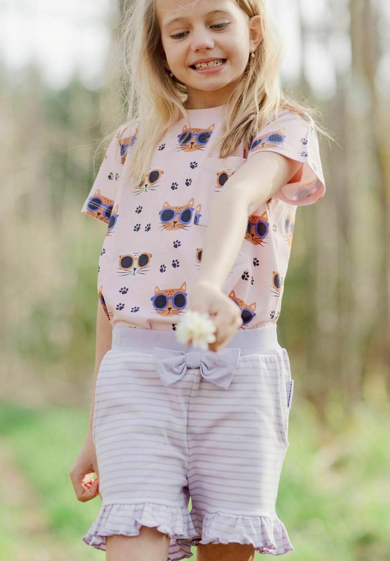 Vaaleanpunainen t-paita, jossa on kissakuviot ja tassunjälkiä; laventelinraidalliset shortsit, joissa on röyhelöitä ja nuppineulan yksityiskohta vyötäröllä.