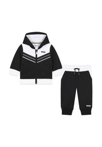 Ensemble de survêtement pour enfants en noir et blanc, comprenant une veste à capuche zippée avec un motif rayé et un pantalon fuselé assorti avec cordon de serrage.