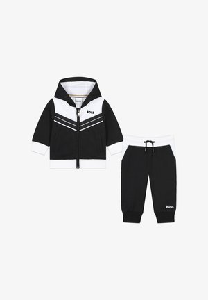 Completo per bambini in bianco e nero, composto da una giacca con cappuccio e zip con motivo a righe e pantaloni tapered abbinati con cordoncino.