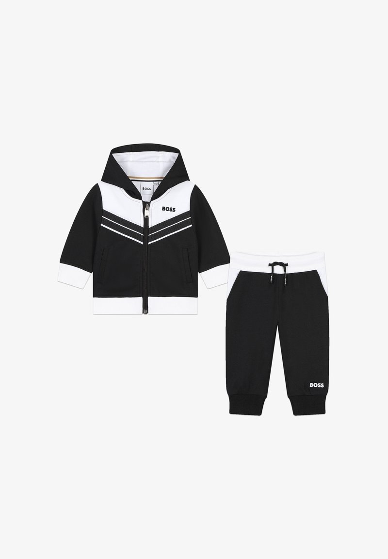 Completo per bambini in bianco e nero, composto da una giacca con cappuccio e zip con motivo a righe e pantaloni tapered abbinati con cordoncino.