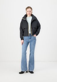 Črn skrajšan jopič z visokim ovratnikom in elastičnimi manšetami, ki ima rumen zadrgo. Nosi se preko svetlo modre majice in modrih širokih hlač.