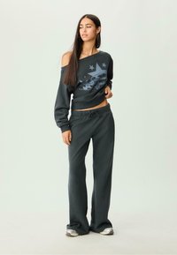 Donkergrijze sweatshirt met een off-shoulder ontwerp, met een autografiek en sterren. Gecombineerd met bijpassende donkergrijze, loose-fitting sweatpants.