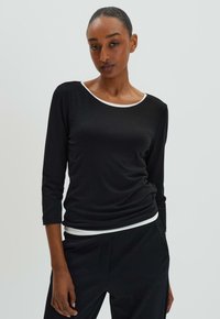 Haut noir à manches longues avec un col rond et une bordure blanche. Fabriqué en tissu lisse, il présente une coupe décontractée avec des manches 3/4.