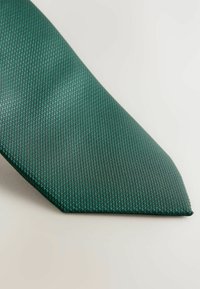Cravate verte à texture avec un tissage à motif subtil, présentant une pointe arrondie et une finition lisse, sur fond clair.