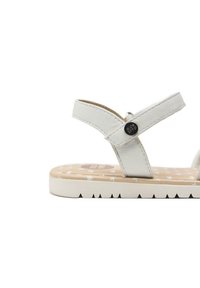 Sandali bianchi in pelle con cinturini incrociati, suola piatta testurizzata con motivi a stella e un accento con logo rotondo sul cinturino.