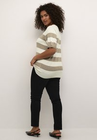 Pulover scurt cu mânecă raglan în dungi, de culoare crem deschis și taupe, cu o croială lejeră și slituri laterale, asortat cu blugi negri skinny și pantofi slingback negri.