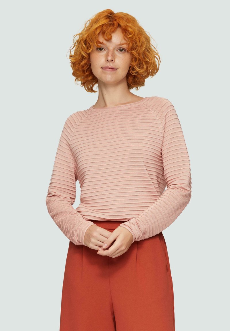 Haut rose clair à manches longues avec texture côtelée horizontale, encolure ras du cou et silhouette ajustée, associé à un pantalon taille haute de couleur rouille.