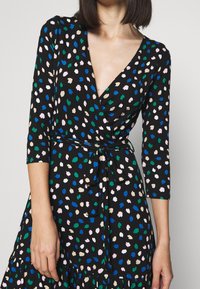 Svart omslagsklänning med V-ringning och trekvartslånga ärmar, prydd med ett flerfärgat stänkmönster. Inkluderar ett självknutet bälte.