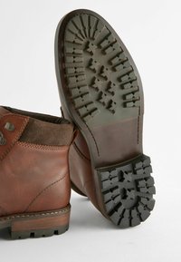 Bruine leren enkelaars met suede accenten en een robuuste rubberen zool met een gepatternde profiel voor grip. Gestikte details langs de rand.
