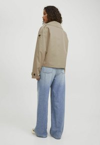 Giacca beige, corta, con un ampio colletto e dettagli con bottoni, abbinata a jeans in denim azzurri, a vestibilità morbida.