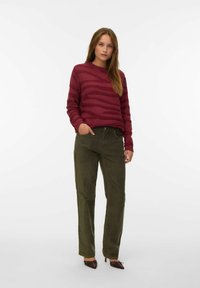 Bordeaux gestreepte trui met geribbelde manchetten, gecombineerd met olijfgroene corduroy broek. Bruine hakken maken de outfit compleet.