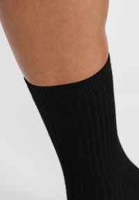 Calcetín negro acanalado hecho de material suave, con un puño alto que se extiende por encima del tobillo. Textura suave, sin patrones ni acentos visibles.