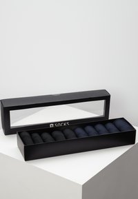 Boîte cadeau noire avec un couvercle transparent contenant huit paires de chaussettes roulées dans différentes nuances de bleu et de noir. Tissu doux, forme uniforme.